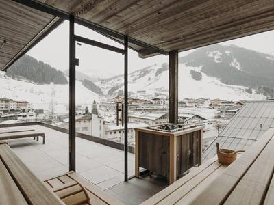 Offene Holzbalkon mit Blick auf schneebedeckte Berge und Dorf unter bewölktem Himmel.