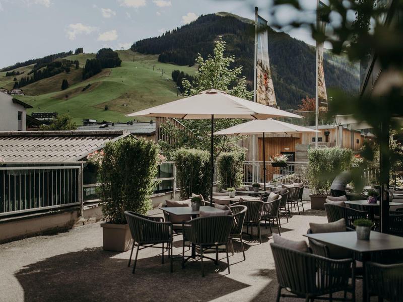 Dachterrasse mit Außensitzplätzen, Sonnenschirmen und Bergblick unter blauem Himmel.