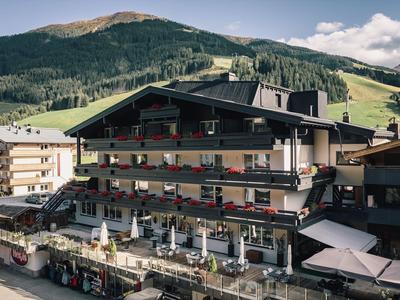 Edificio dell'hotel con balconi e area esterna davanti a un paesaggio montano boscoso.