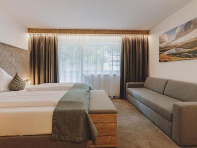 Camera d'hotel moderna con letto matrimoniale, divano e ampia finestra con tende.