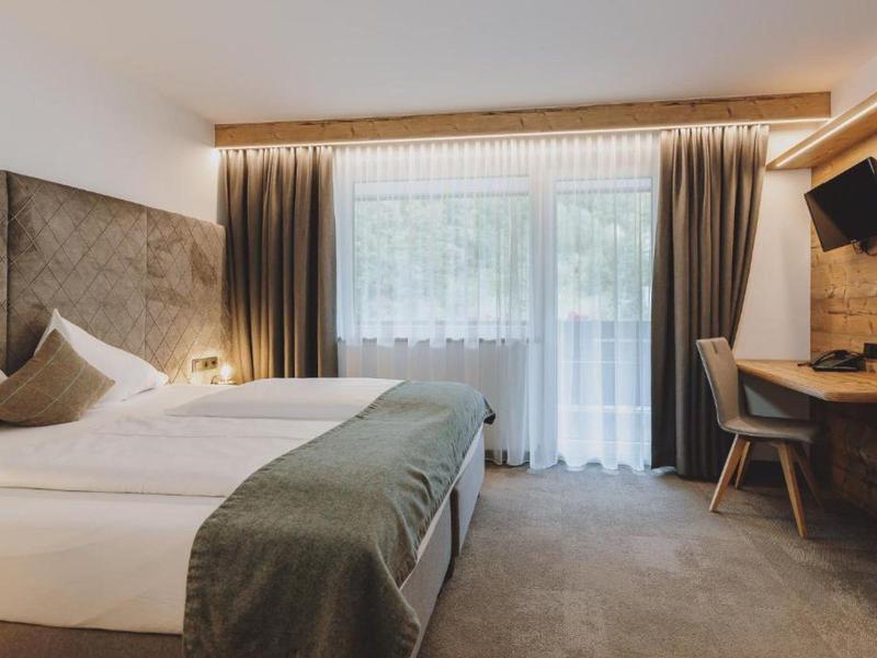 Camera d'hotel luminosa con letto matrimoniale, grandi tende e scrivania con televisore.