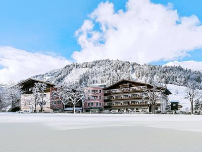 Schneebedecktes Hotelgebäude vor einem bewaldeten Berg unter blauem Himmel mit Wolken