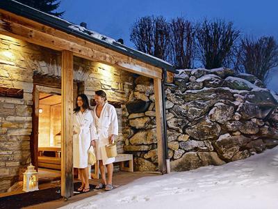 Paar in Bademänteln verlässt ein beleuchtetes Steinhaus im Schnee bei Nacht.
