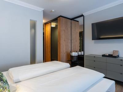 Modern eingerichtetes Hotelzimmer mit Doppelbett, großem TV und Schrank mit Holztüren