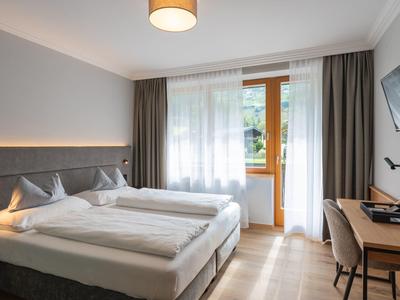 Modernes Hotelzimmer mit zwei Betten, Schreibtisch und Balkon mit Blick ins Grüne.