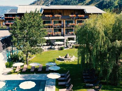 Hotel mit Garten, Pool, Liegestühlen und Bergblick an einem sonnigen Tag.