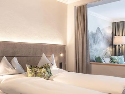 Gemütliches Hotelzimmer mit zwei Betten, großem Kopfteil und Blick auf dekoratives Wandbild.