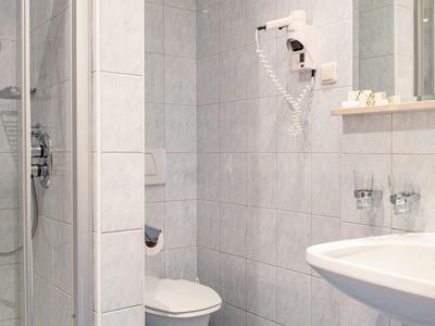 Kleines Hotelbad mit Dusche, Toilette, Waschbecken und Haartrockner an der Wand