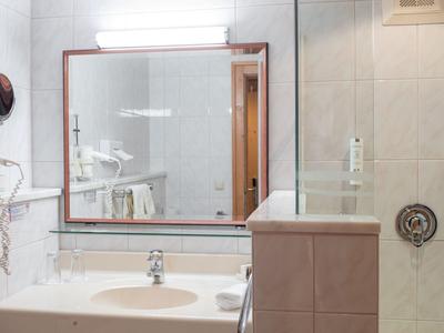 Modernes Badezimmer mit großem Spiegel, Waschbecken und hellen Fliesen.