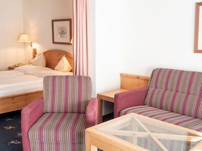 Gemütliche Hotellounge mit gestreiftem Sessel, Sofa und Holztisch mit Glasplatte.