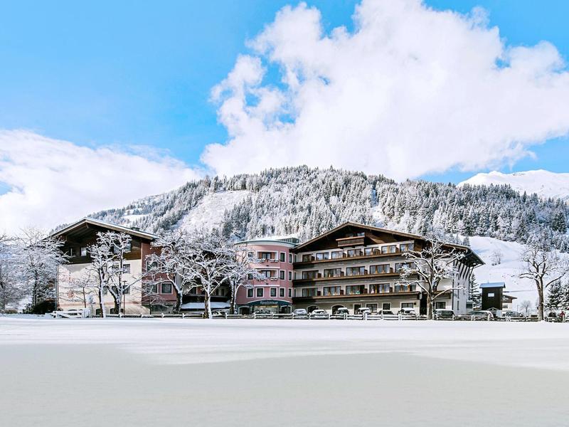 Schneebedecktes Hotelgebäude vor einem bewaldeten Berg unter blauem Himmel mit Wolken