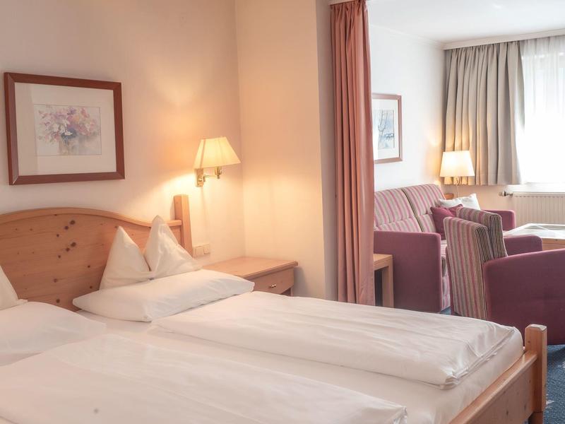 Hell eingerichtetes Hotelzimmer mit zwei Einzelbetten und Sitzbereich im Hintergrund.