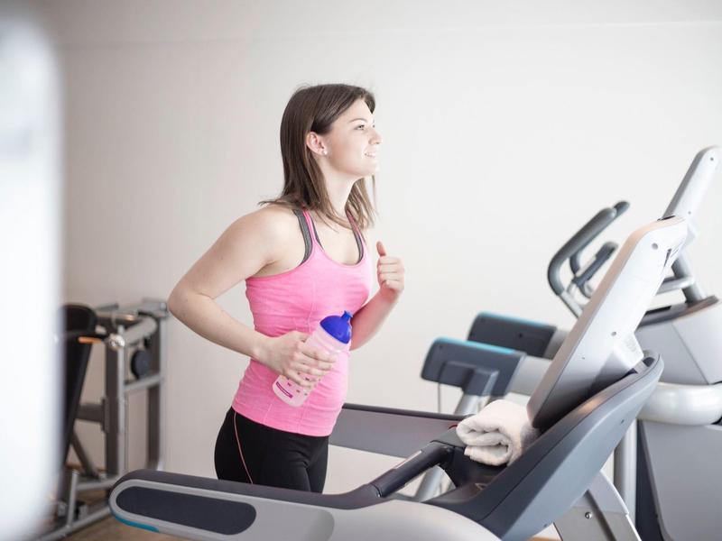 Frau in Sportkleidung trainiert auf Laufband im Fitnessraum eines Hotels