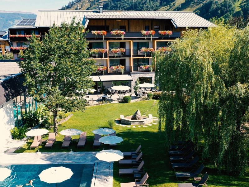 Hotel mit Garten, Pool, Liegestühlen und Bergblick an einem sonnigen Tag.