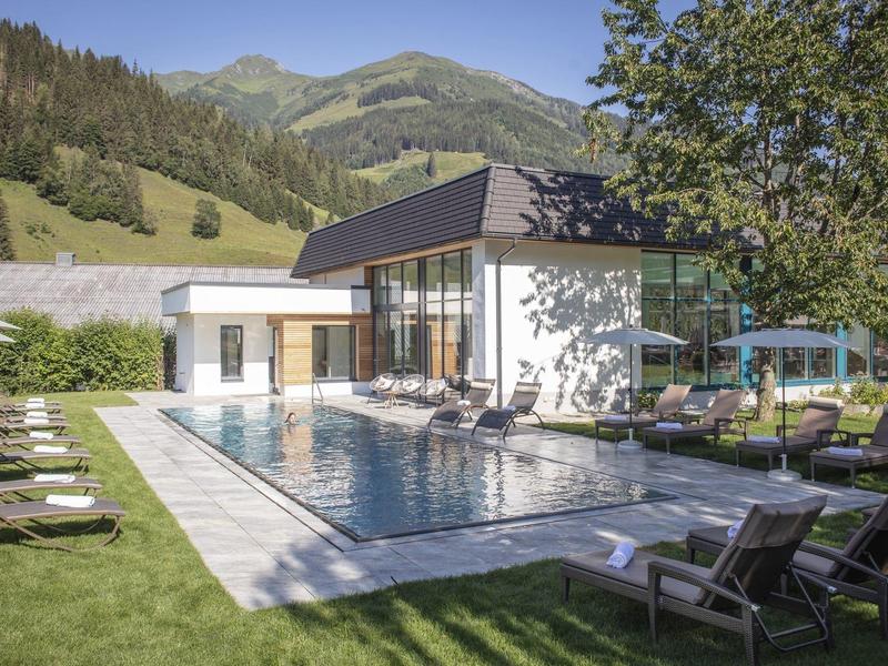 Moderner Swimmingpool mit Liegestühlen vor einem Hotel in den Bergen bei Sonnenschein.