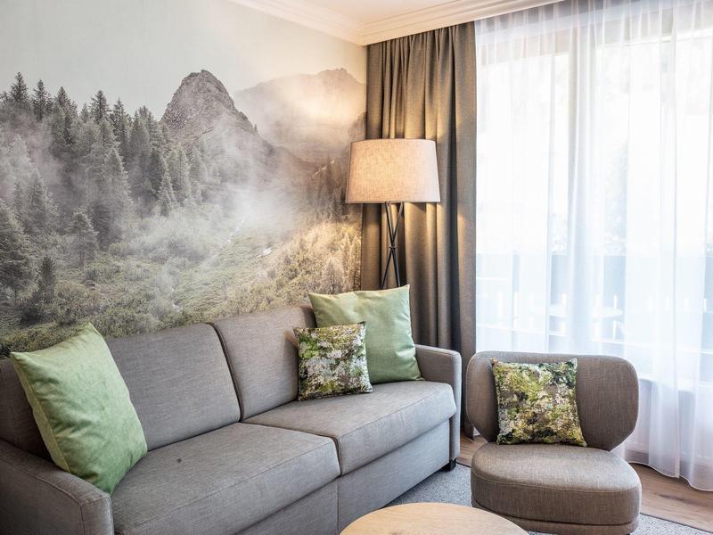 Modernes Wohnzimmer mit grauem Sofa, grünlichen Kissen, Stehlampe und Wald-Wandbild.