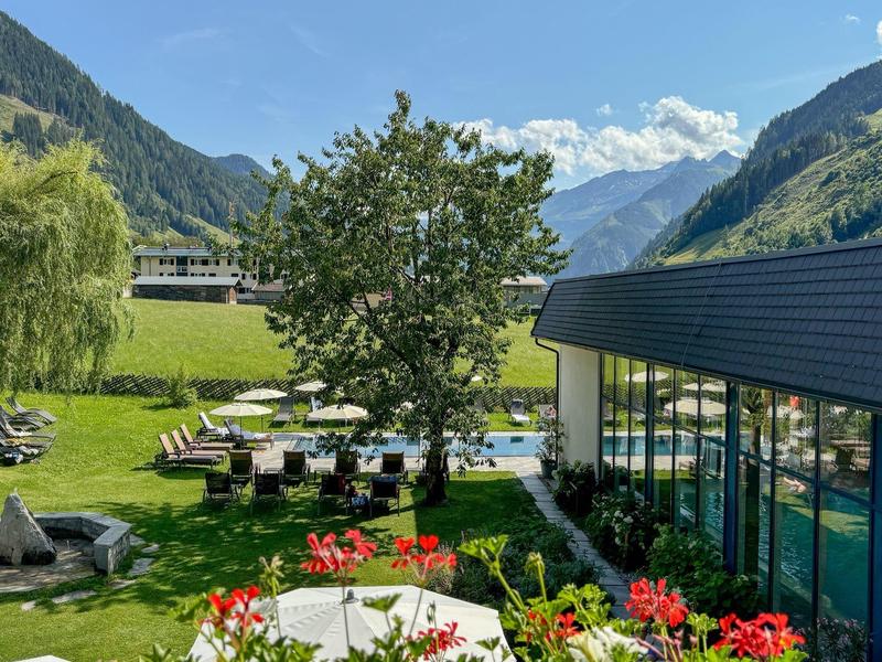 Grüne Wiese mit Blumen, Bäumen und Blick auf Berge neben einem modernen Glasgebäude.
