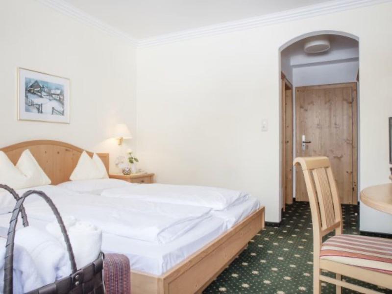 Schlichtes Schlafzimmer mit Holzbett, Nachttischlampe, grünem Teppich und Holzstuhl am Tisch.