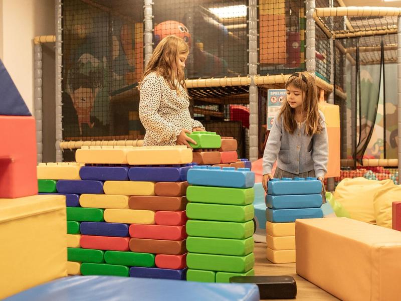 Zwei Mädchen bauen bunte Schaumstoffblöcke in einem Indoor-Spielbereich mit Klettergerüst.