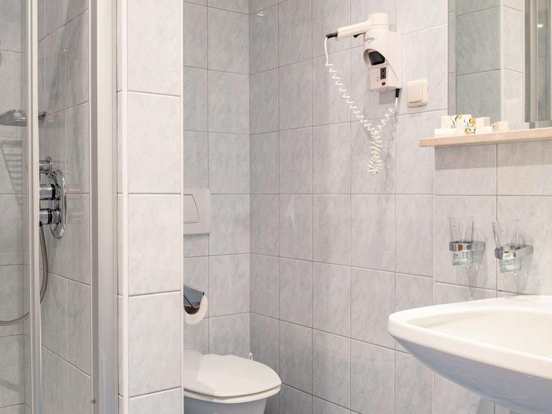 Kleines Hotelbad mit Dusche, Toilette, Waschbecken und Haartrockner an der Wand