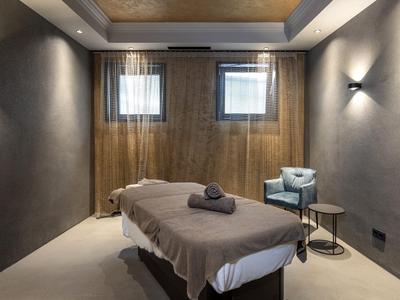 Modern eingerichteter Wellnessraum mit Massageliege, Sessel und gedämpfter Beleuchtung.