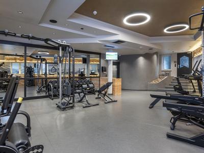 Moderner Fitnessraum mit verschiedenen Geräten und beleuchtetem Decken-Design im Hotel.