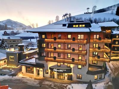 Hotelgebäude im Schnee mit warm beleuchteten Fenstern und Bergkulisse bei Dämmerung.