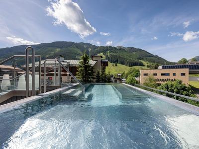Außenpool mit sprudelndem Wasser, umgeben von Bergen und Hotels bei klarem Himmel.