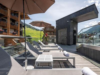 Sonnenterrasse mit grauen Liegestühlen, Holzboden und Bergblick an einer Hotelanlage.