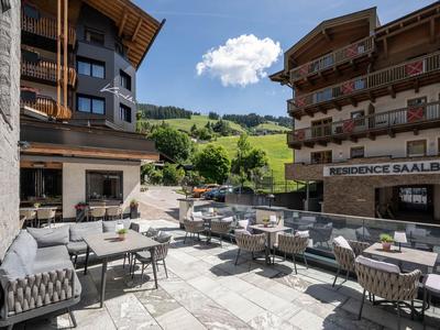 Terrasse eines Hotels mit Tischen und Stühlen vor Bergwiesen und Hügeln im Hintergrund.