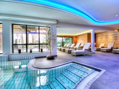 Moderner Wellnessbereich mit Whirlpool, Liegen und indirekter blauer Deckenbeleuchtung.