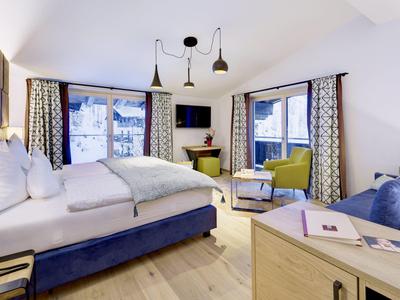 Przytulny pokój hotelowy z dużym łóżkiem, fotelami i widokiem na ośnieżone góry.