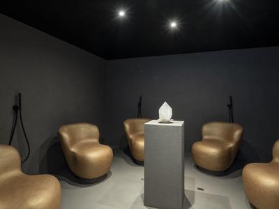 Moderne Sitzecke mit braunen Sesseln und Skulptur auf einem Sockel in dunklem Raum