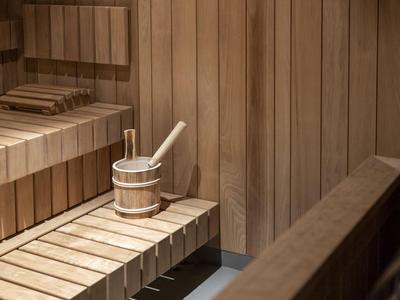 Holzsauna mit Bank und Wassereimer mit Schöpfer in einem ruhigen Raum.