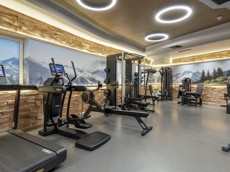 Nowoczesna siłownia z urządzeniami cardio i siłowymi, panoramiczne okna z widokiem na góry.