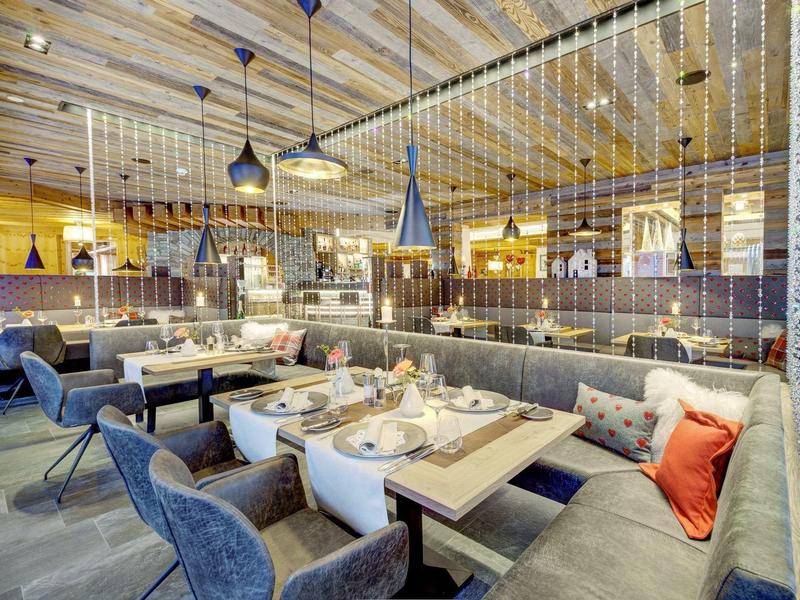 Nowoczesne wnętrze restauracji z nakrytymi stołami, wygodnymi fotelami i sofami w ciepłym oświetleniu.