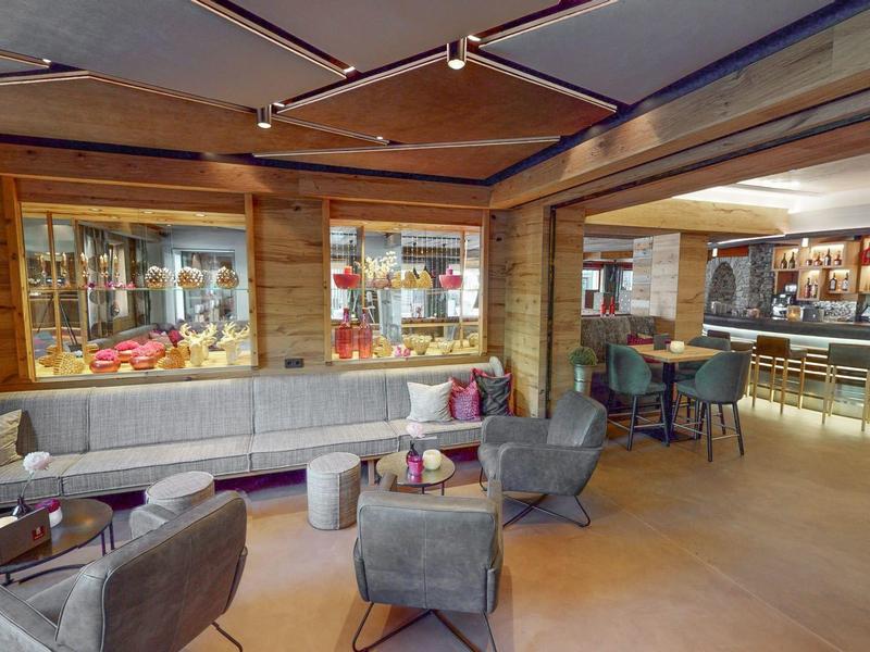 Przytulny bar hotelowy z wygodnymi fotelami, długimi sofami i oświetlonym barem.