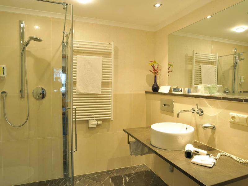 Nowoczesna łazienka z prysznicem, dużym lustrem i umywalką na szarym blacie.