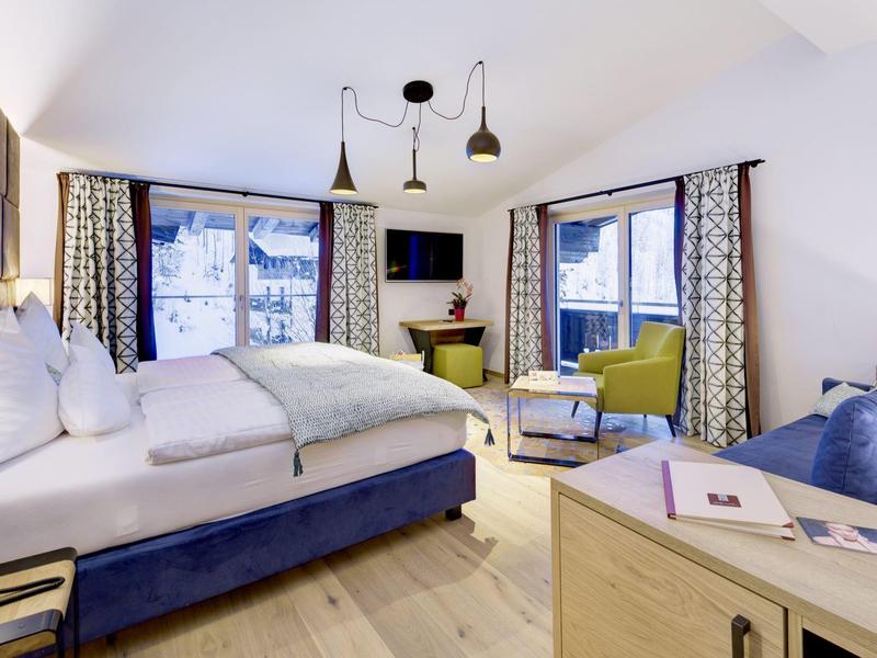 Przytulny pokój hotelowy z dużym łóżkiem, fotelami i widokiem na ośnieżone góry.