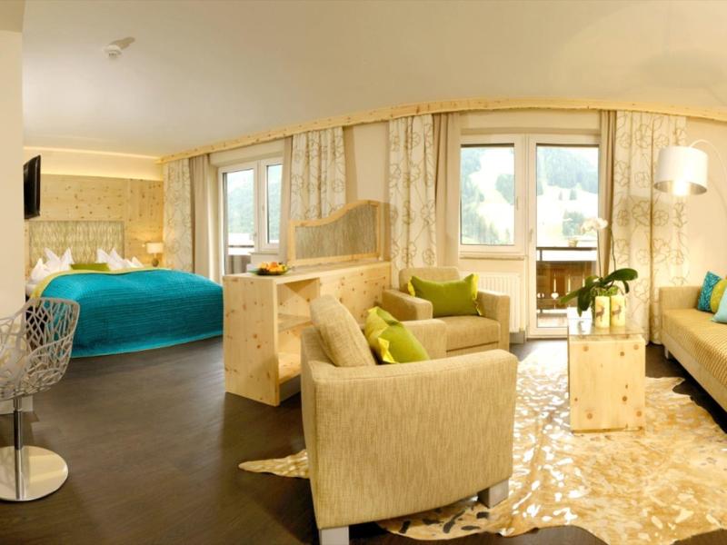 Jasny, nowoczesny pokój hotelowy z częścią wypoczynkową i dużymi oknami.