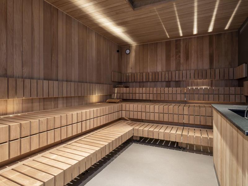 Nowoczesna sauna z piętrowymi drewnianymi ławkami i pośrednim oświetleniem sufitowym.
