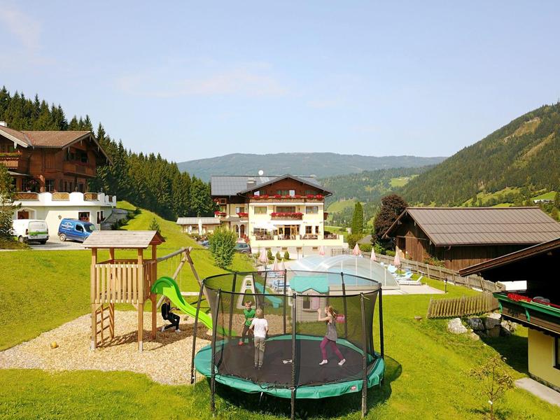 Station de montagne avec aire de jeux, trampoline et piscine extérieure entourée de collines verdoyantes.