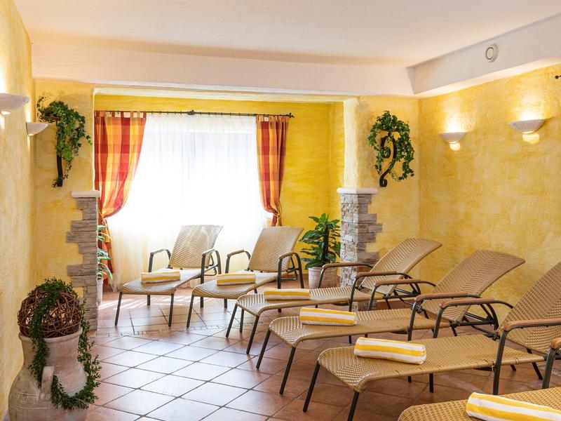 Espace bien-être confortable avec chaises longues, fauteuils, plantes et sol carrelé clair.