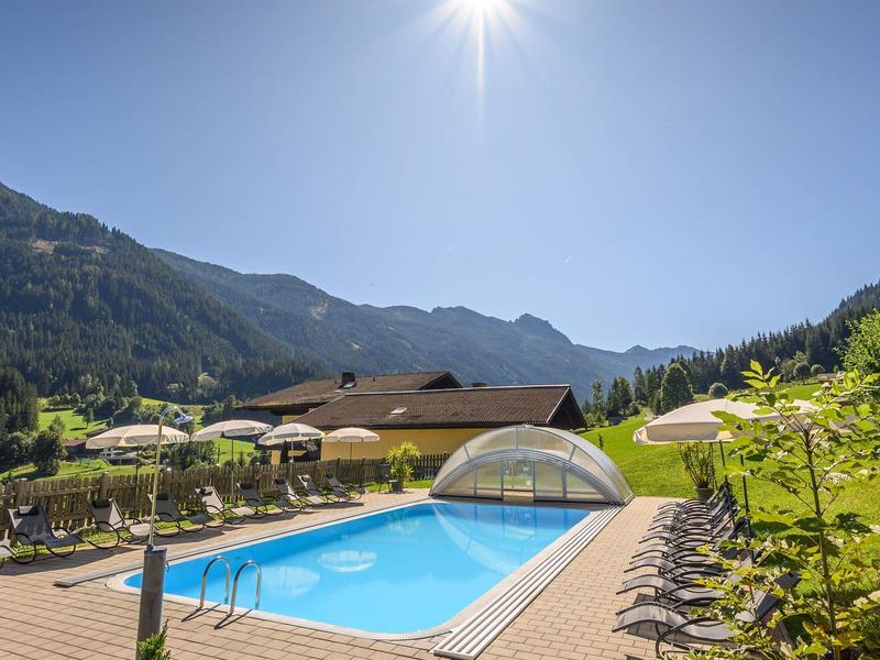 Piscine ensoleillée avec chaises longues dans un cadre montagneux près d'un hôtel.