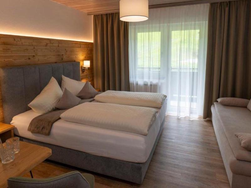 Chambre d'hôtel confortable avec deux lits simples, canapé et balcon avec rideaux.