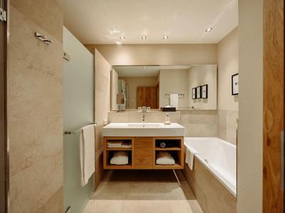 Jasna łazienka z dużą wanną, umywalką, lustrem i jasnymi płytkami.