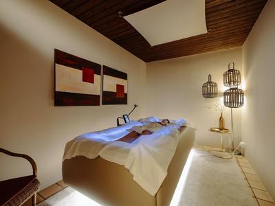 Przytulny pokój wellness z leżanką do masażu, ciepłym oświetleniem i drewnianym sufitem.