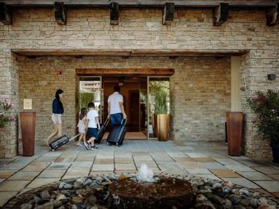 Famiglia con passeggino e valigie che entra in un ingresso d'hotel con pareti in pietra e grande portone.