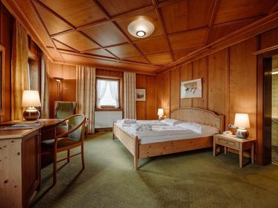 Przytulny pokój hotelowy z drewnianymi panelami, podwójnym łóżkiem i zielonym dywanem