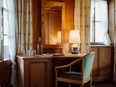 Drewniane biurko z krzesłem, lampą i lustrem między dwoma oknami w przytulnym pokoju hotelowym.